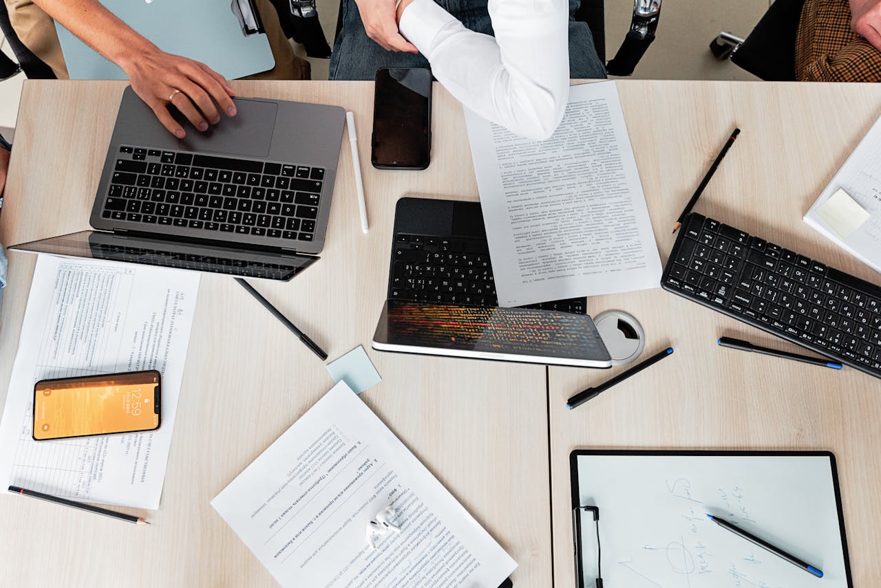 About Overhead shot of office desk with laptops, documents, and tech gadgets during a business meeting.